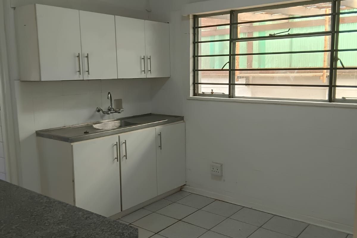A functional, empty kitchen space featuring white built-in cabinetry, a stainless steel sink, and tiled flooring, ready for modernization.