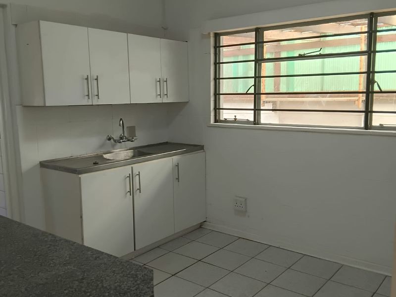 A functional, empty kitchen space featuring white built-in cabinetry, a stainless steel sink, and tiled flooring, ready for modernization.