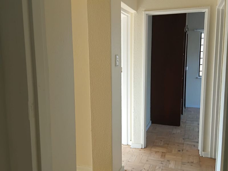 A bright hallway featuring classic parquet flooring and an archway, providing access to adjacent rooms and a ceiling hatch.