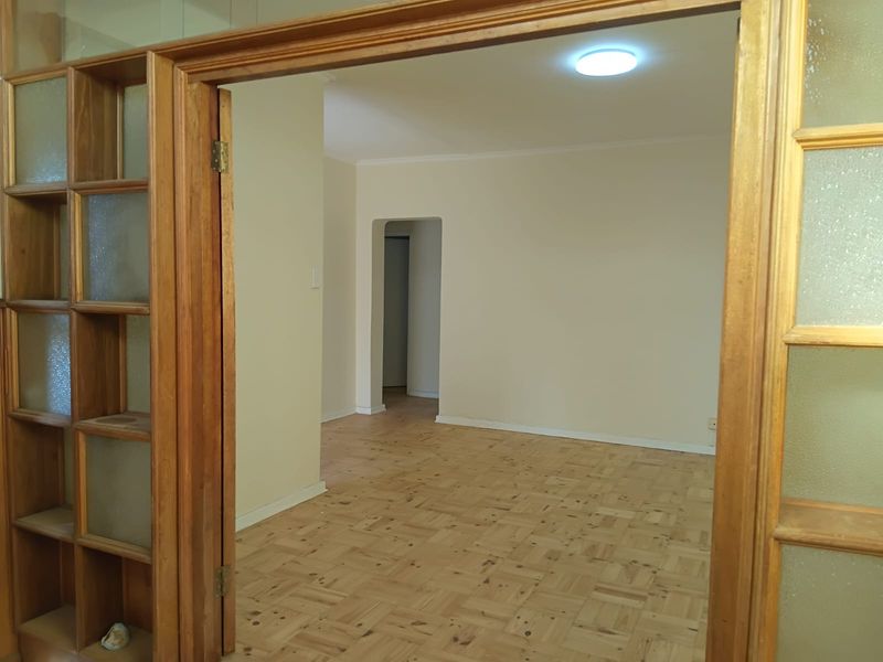 An empty living room featuring classic parquet flooring, timber-framed glass doors, and a built-in wooden shelving unit, offering a neutral canvas for interior design.