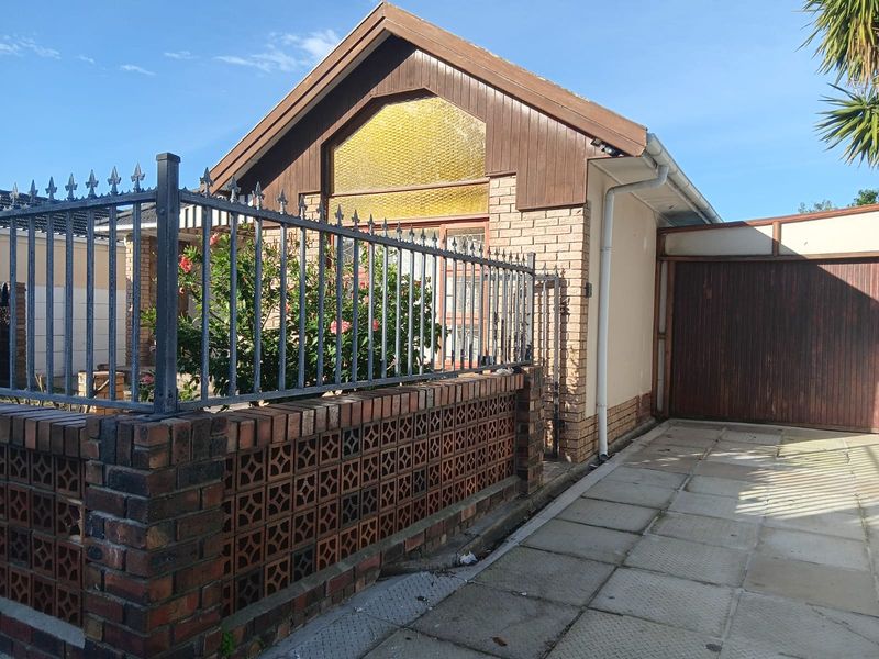 Front exterior view of a brick house featuring a paved driveway, garage, and decorative brick and metal security fencing.