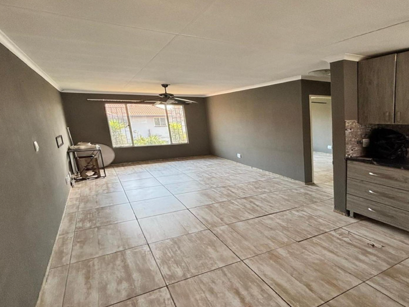 Spacious open-plan living area featuring tiled flooring, a ceiling fan, and a modern kitchen with built-in cabinetry, oven, and hob.