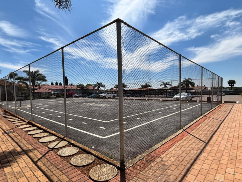 A fenced outdoor sports court with asphalt surfacing and surrounding paved walkways, located within the apartment complex grounds.
