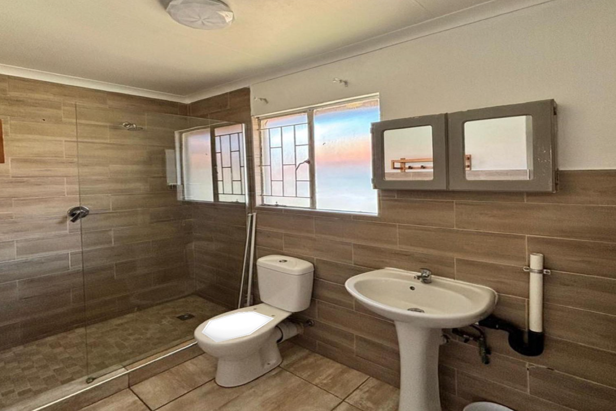 A functional bathroom featuring a walk-in shower with glass screen, pedestal basin, and toilet, finished with neutral wall and floor tiles.