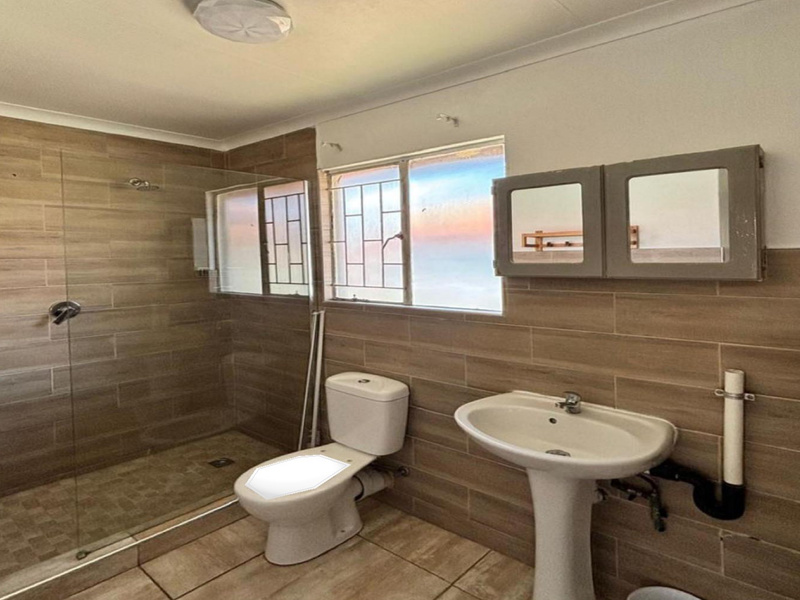 A functional bathroom featuring a walk-in shower with glass screen, pedestal basin, and toilet, finished with neutral wall and floor tiles.