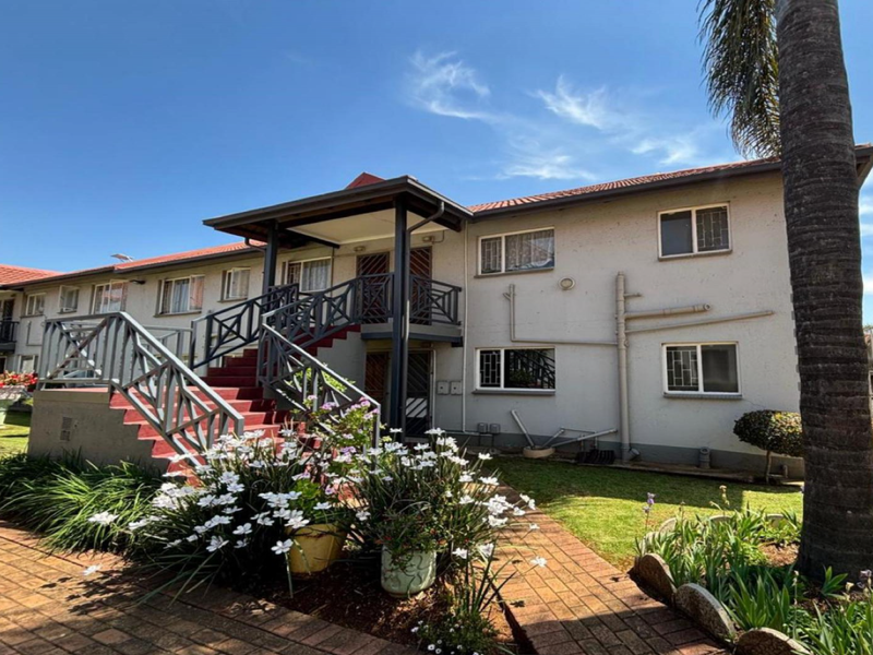 Exterior view of an apartment complex featuring a staircase, paved walkways, and landscaped garden area under a clear blue sky.