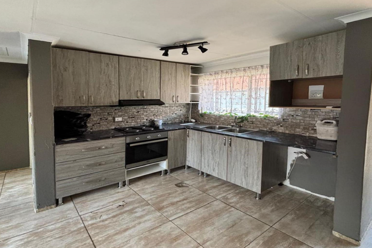 A functional kitchen featuring wood-look cabinetry, built-in oven and hob, double sink, and tiled flooring, offering a practical layout for culinary activities.