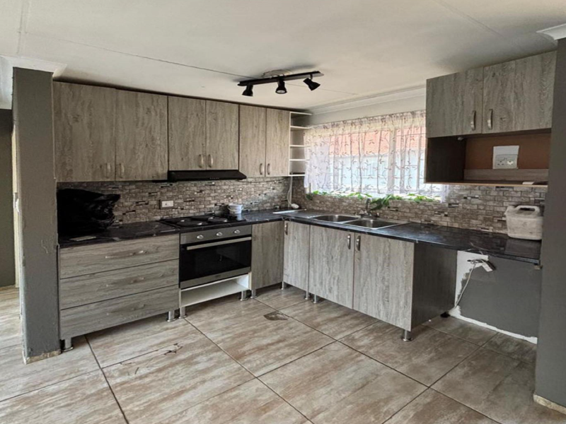 A functional kitchen featuring wood-look cabinetry, built-in oven and hob, double sink, and tiled flooring, offering a practical layout for culinary activities.