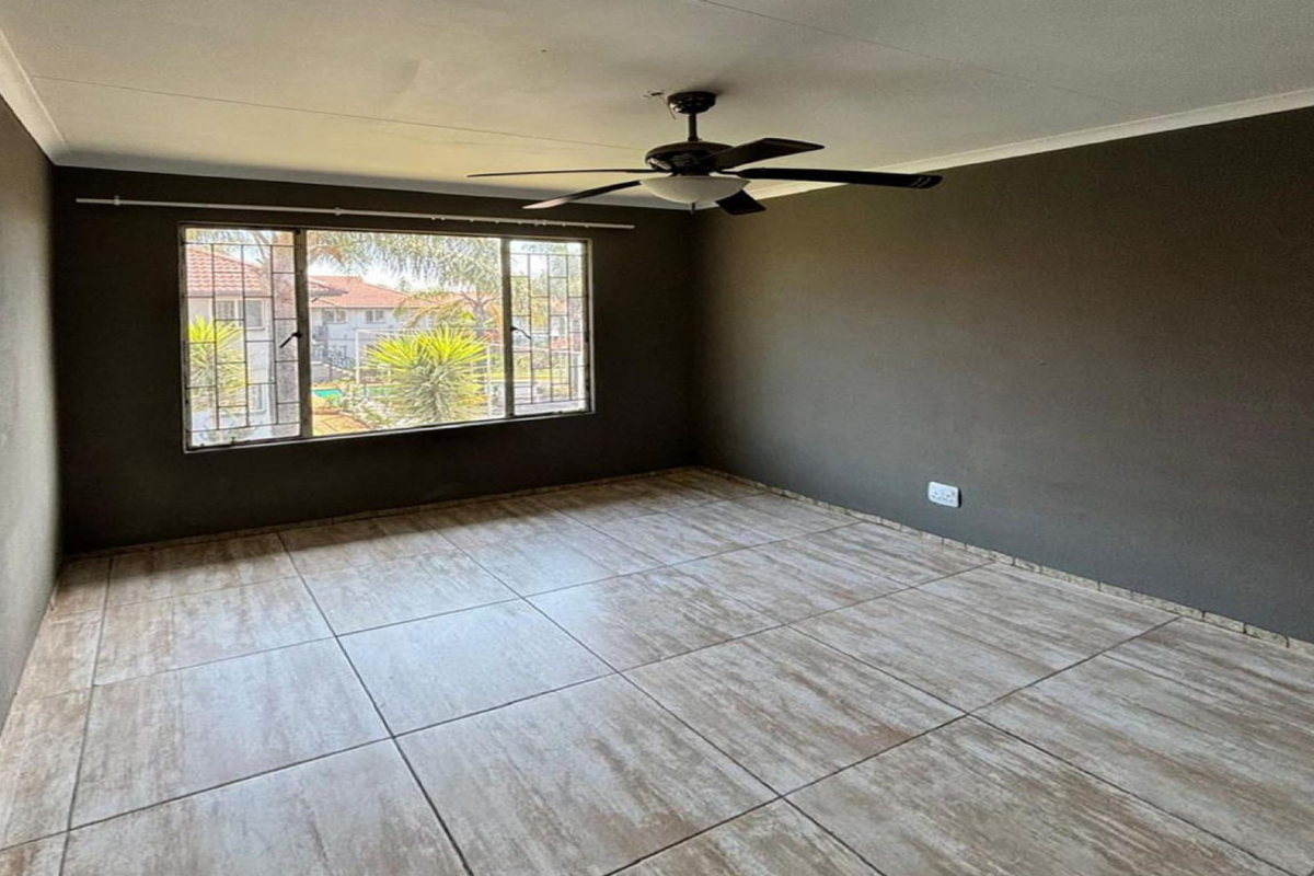 A spacious, empty living room featuring neutral tiled flooring, dark painted walls, and a ceiling fan, offering a blank canvas for personalization.