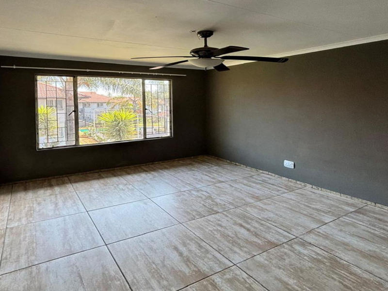 A spacious, empty living room featuring neutral tiled flooring, dark painted walls, and a ceiling fan, offering a blank canvas for personalization.