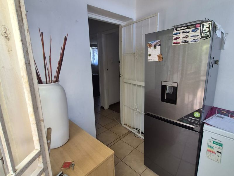 A utility or scullery area featuring tiled flooring and a security gate, currently requiring ceiling completion and general maintenance.