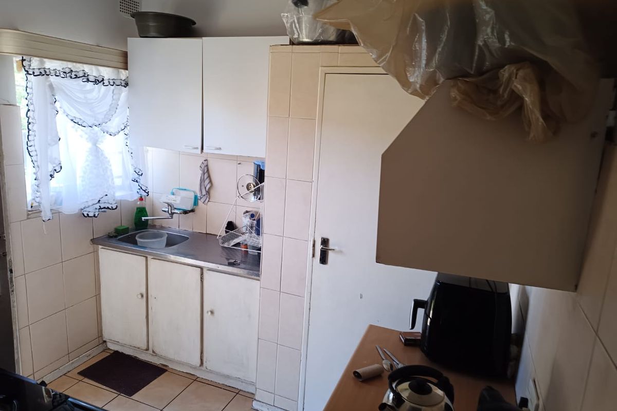 A compact kitchen featuring built-in cabinetry, a stainless steel sink, and tiled splashbacks, offering a functional space with potential for modernization.