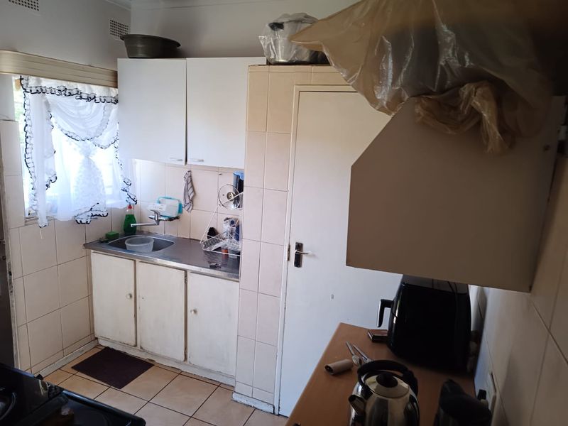 A compact kitchen featuring built-in cabinetry, a stainless steel sink, and tiled splashbacks, offering a functional space with potential for modernization.