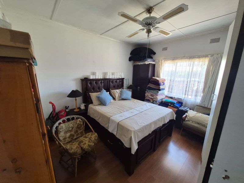A bedroom featuring laminate flooring and a ceiling fan, currently showing signs of wear including visible ceiling panel damage.