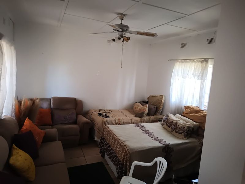 A bedroom featuring tiled flooring, a ceiling fan, and ventilation bricks, with visible wear on the ceiling panels.