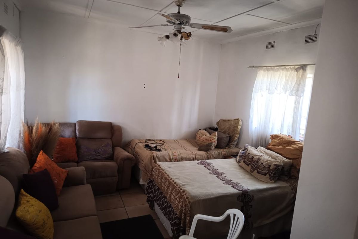 A living area featuring tiled flooring and a ceiling fan, currently utilized as a multi-purpose space with dated finishes.