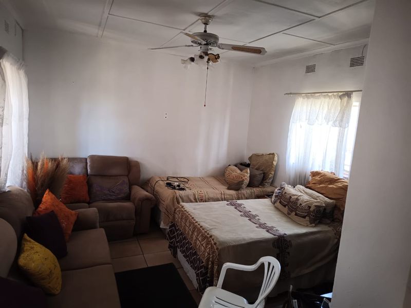 A living area featuring tiled flooring and a ceiling fan, currently utilized as a multi-purpose space with dated finishes.