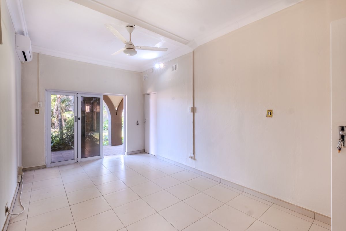 An empty, well-lit living area featuring tiled flooring, a ceiling fan, and a sliding glass door providing access to an outdoor patio space.