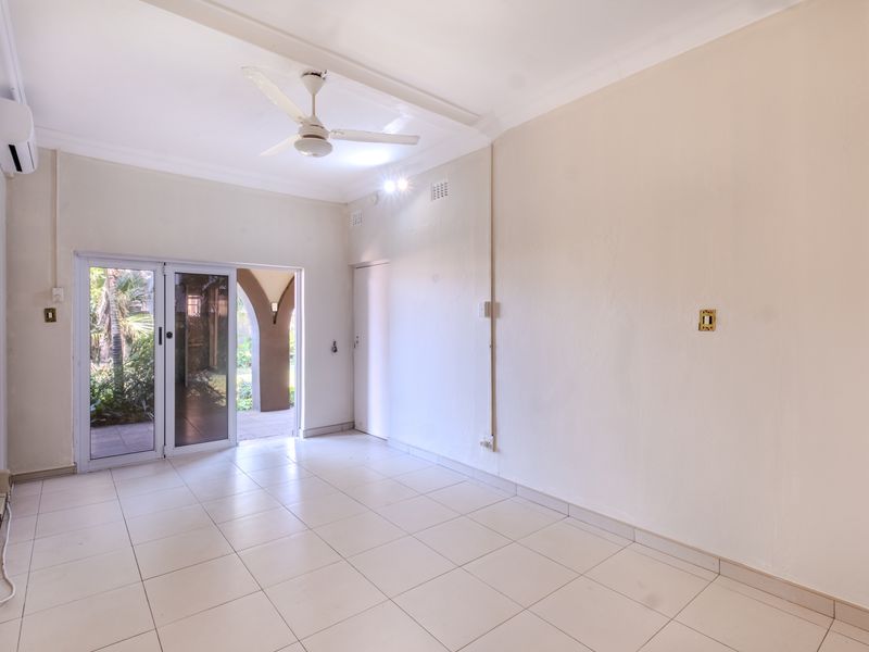 An empty, well-lit living area featuring tiled flooring, a ceiling fan, and a sliding glass door providing access to an outdoor patio space.