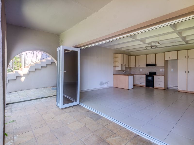 Open-plan kitchen and living area featuring tiled floors, built-in cabinetry, and seamless access to a covered patio through large folding glass doors.