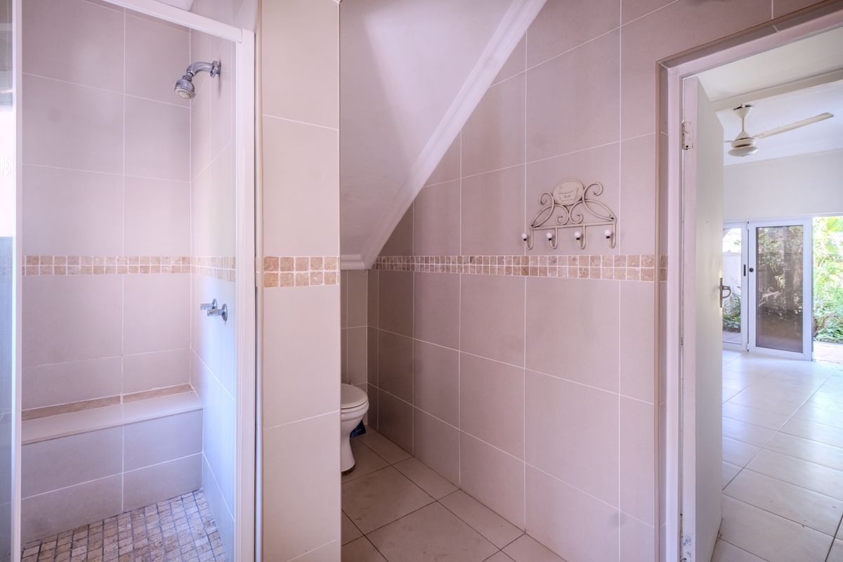A clean, neutral-toned bathroom featuring a walk-in shower with a built-in bench, tiled finishes, and a separate toilet area.