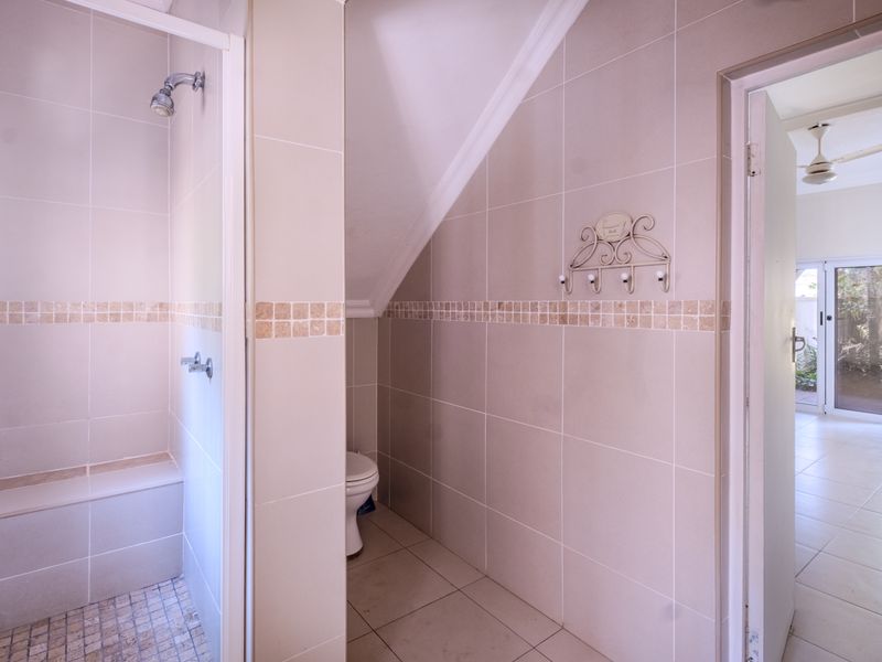 A clean, neutral-toned bathroom featuring a walk-in shower with a built-in bench, tiled finishes, and a separate toilet area.