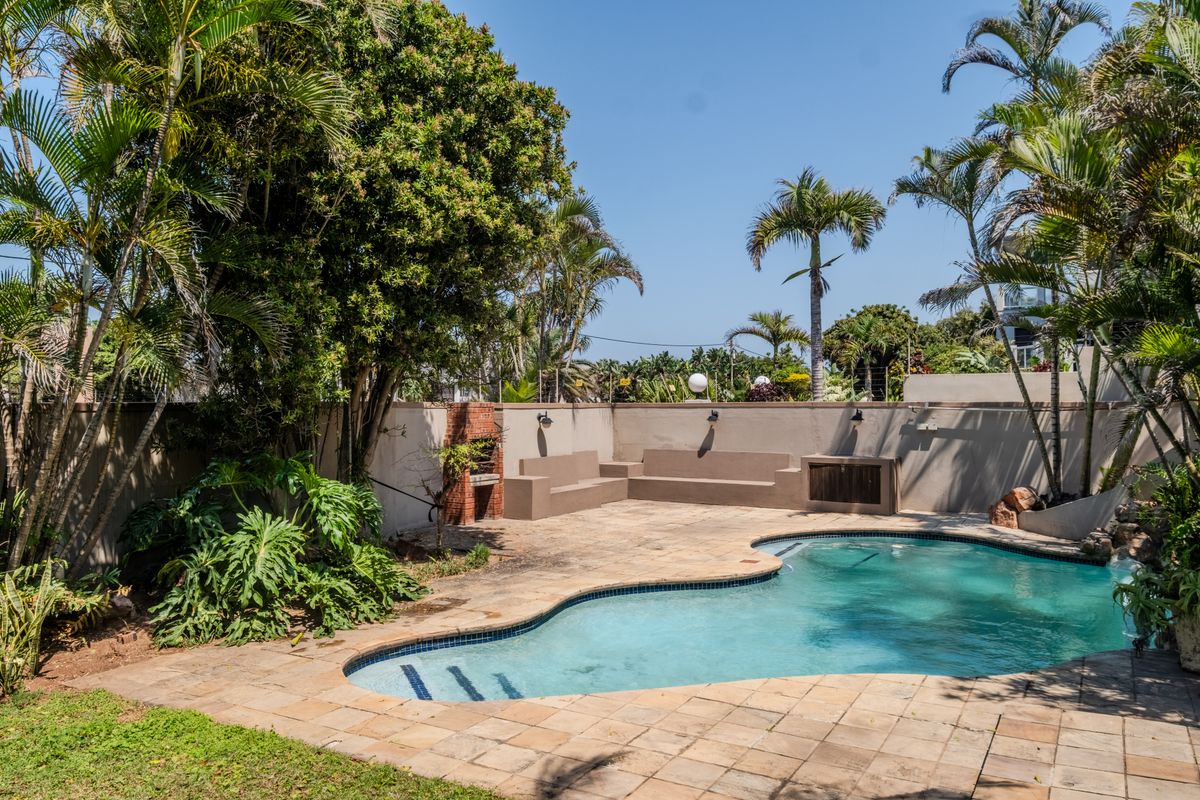 Outdoor pool area featuring a swimming pool, paved deck, built-in brick braai, and integrated concrete seating, surrounded by a private boundary wall and garden.