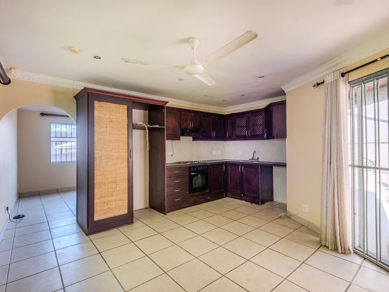 Open plan kitchen area featuring dark wood cabinetry, built-in oven and hob, tiled flooring, and direct access to an outdoor space via a security gate.