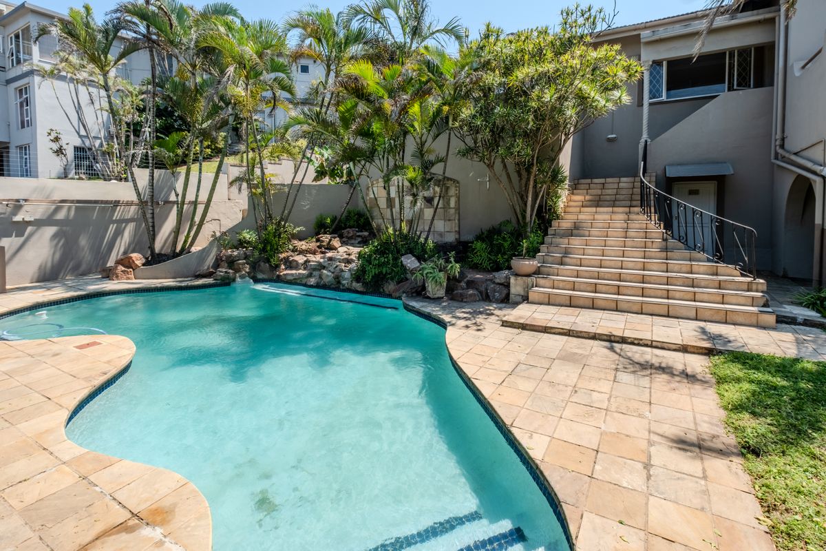 Outdoor pool area featuring a swimming pool, tiled patio, and a stone-accented staircase with wrought iron railings leading to the property entrance.