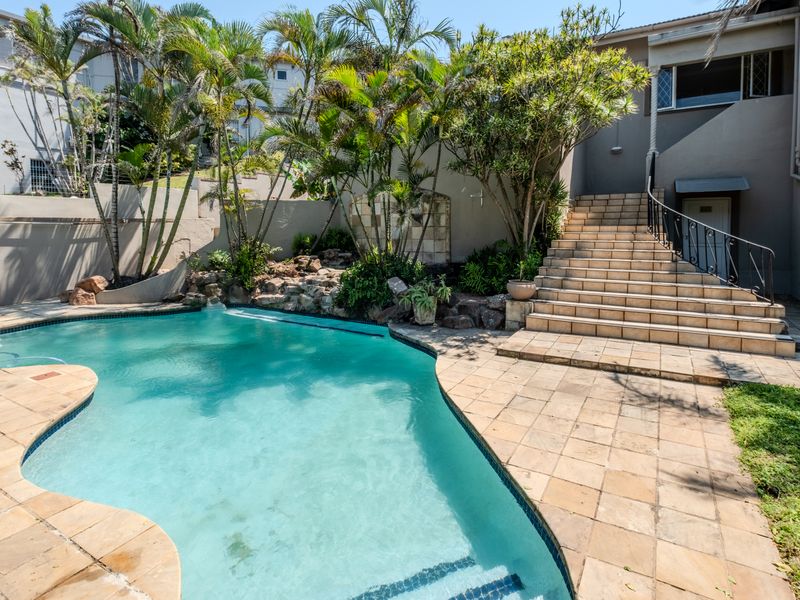 Outdoor pool area featuring a swimming pool, tiled patio, and a stone-accented staircase with wrought iron railings leading to the property entrance.