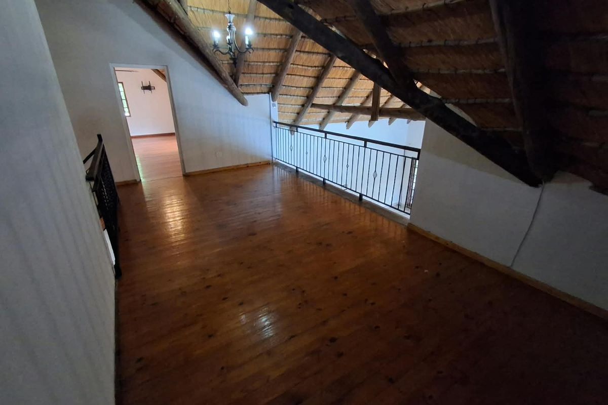 Spacious loft area featuring exposed timber rafters, a traditional thatched roof, and polished timber flooring with a metal balustrade overlooking the lower level.