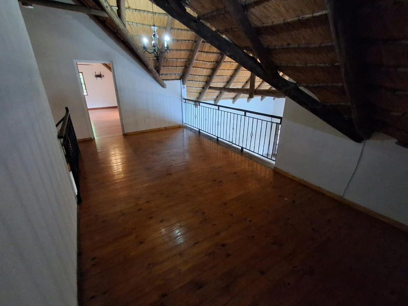 Spacious loft area featuring exposed timber rafters, a traditional thatched roof, and polished timber flooring with a metal balustrade overlooking the lower level.