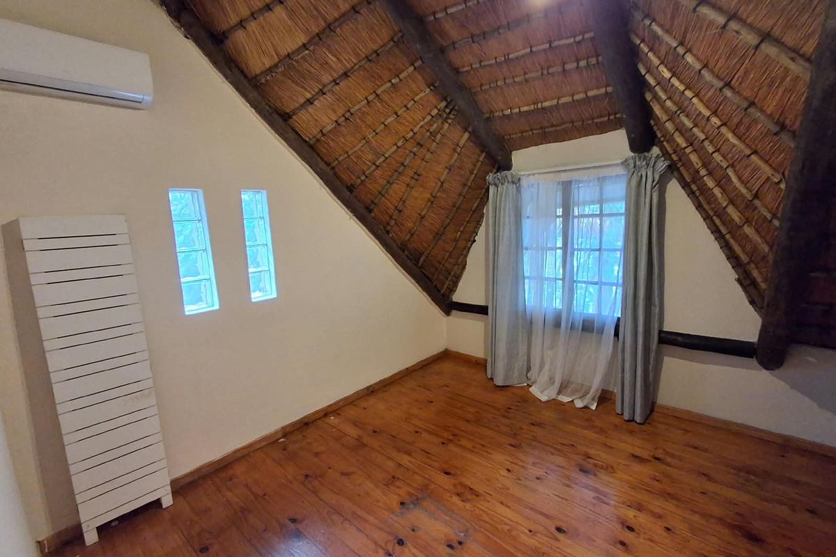 An empty bedroom featuring a vaulted thatch ceiling with exposed timber beams, polished timber flooring, and a wall-mounted air conditioning unit.