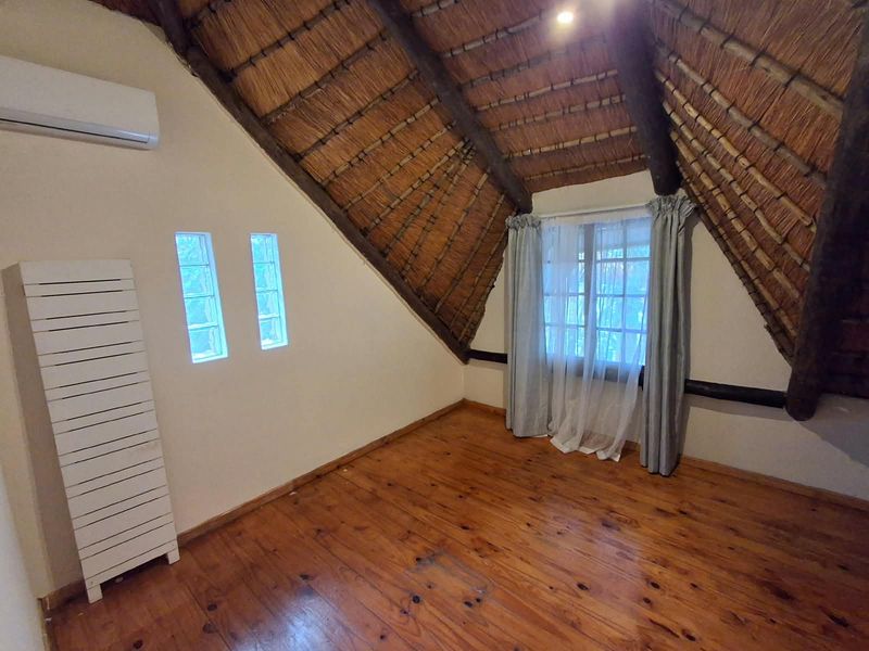 An empty bedroom featuring a vaulted thatch ceiling with exposed timber beams, polished timber flooring, and a wall-mounted air conditioning unit.
