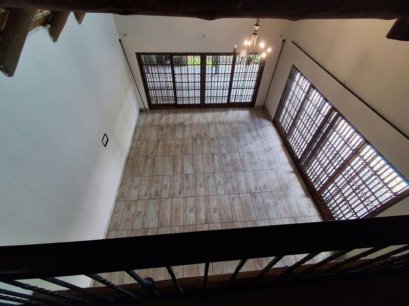 Spacious, empty living area featuring wood-look tiled flooring, high ceilings, and large glass doors with integrated metal security gates.