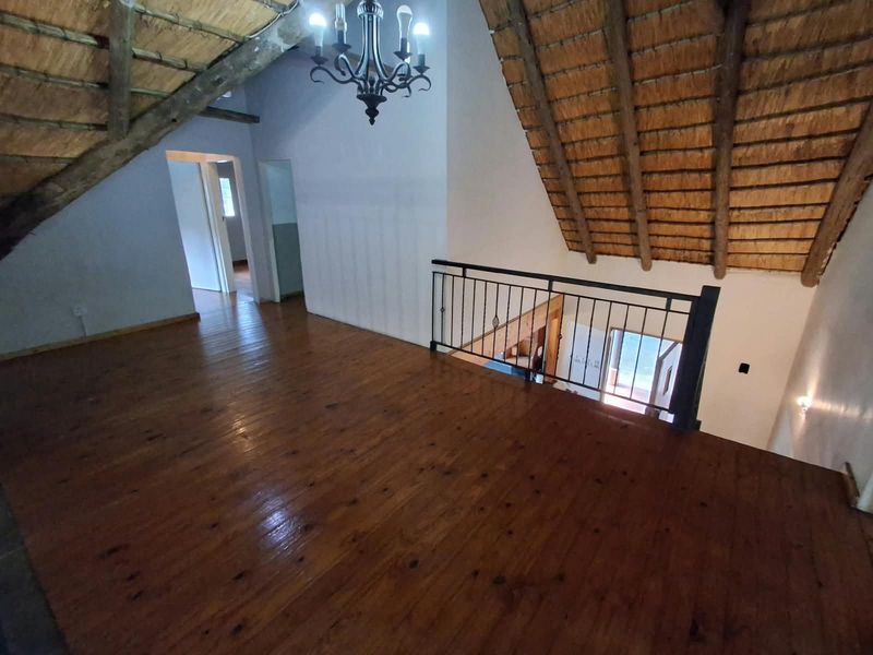 Spacious loft living area featuring exposed thatch roofing, polished timber flooring, and a decorative wrought iron balustrade overlooking the lower level.