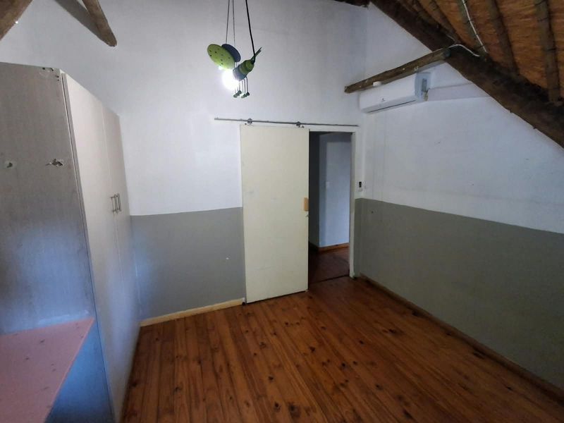 A bedroom featuring exposed timber rafters, a thatch roof, timber flooring, built-in cupboards, and a wall-mounted air conditioning unit.