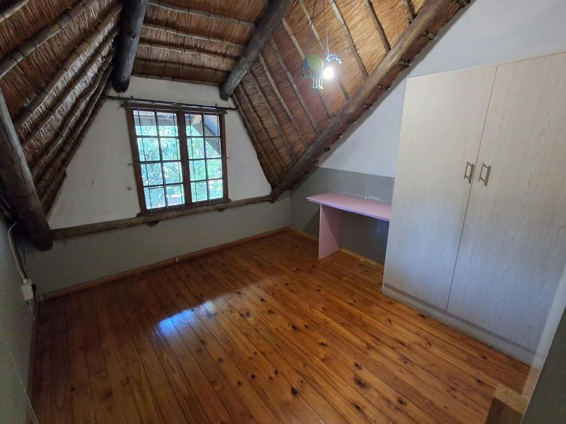 A loft-style bedroom featuring a traditional thatched roof with exposed timber beams, polished timber flooring, and built-in storage and desk space.
