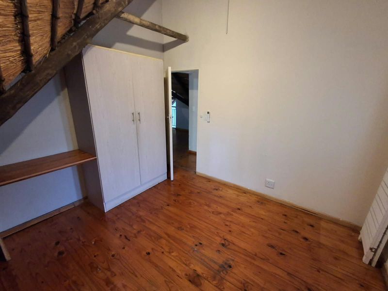 Bedroom featuring timber flooring, built-in wardrobe, and exposed thatch roof detailing.