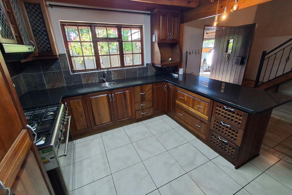 A well-maintained kitchen featuring dark wood cabinetry, granite countertops, a gas stove, and exposed wooden ceiling beams, offering a warm and functional cooking space.