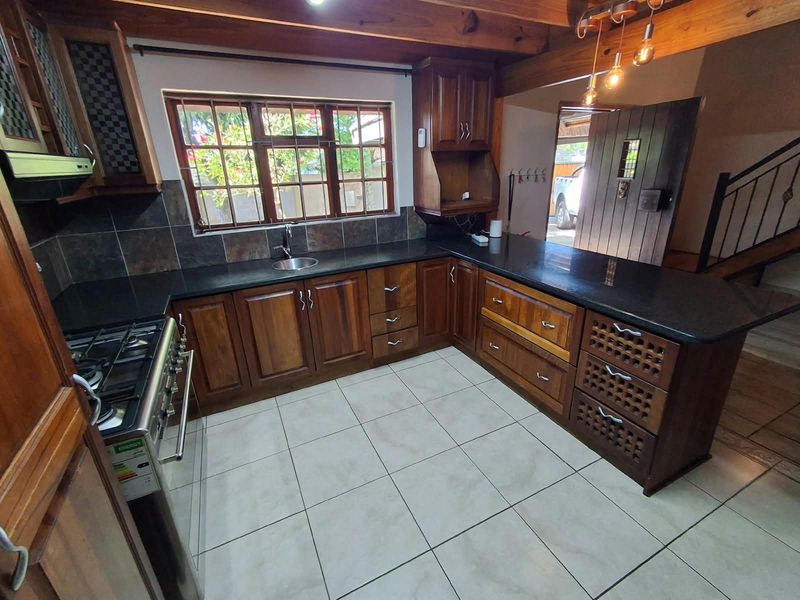 A well-maintained kitchen featuring dark wood cabinetry, granite countertops, a gas stove, and exposed wooden ceiling beams, offering a warm and functional cooking space.