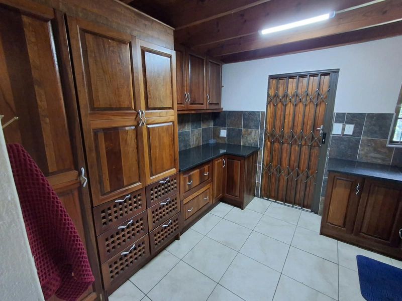 A functional scullery featuring extensive wooden cabinetry, granite countertops, tiled backsplash, and exposed wooden ceiling beams, providing ample storage and workspace.