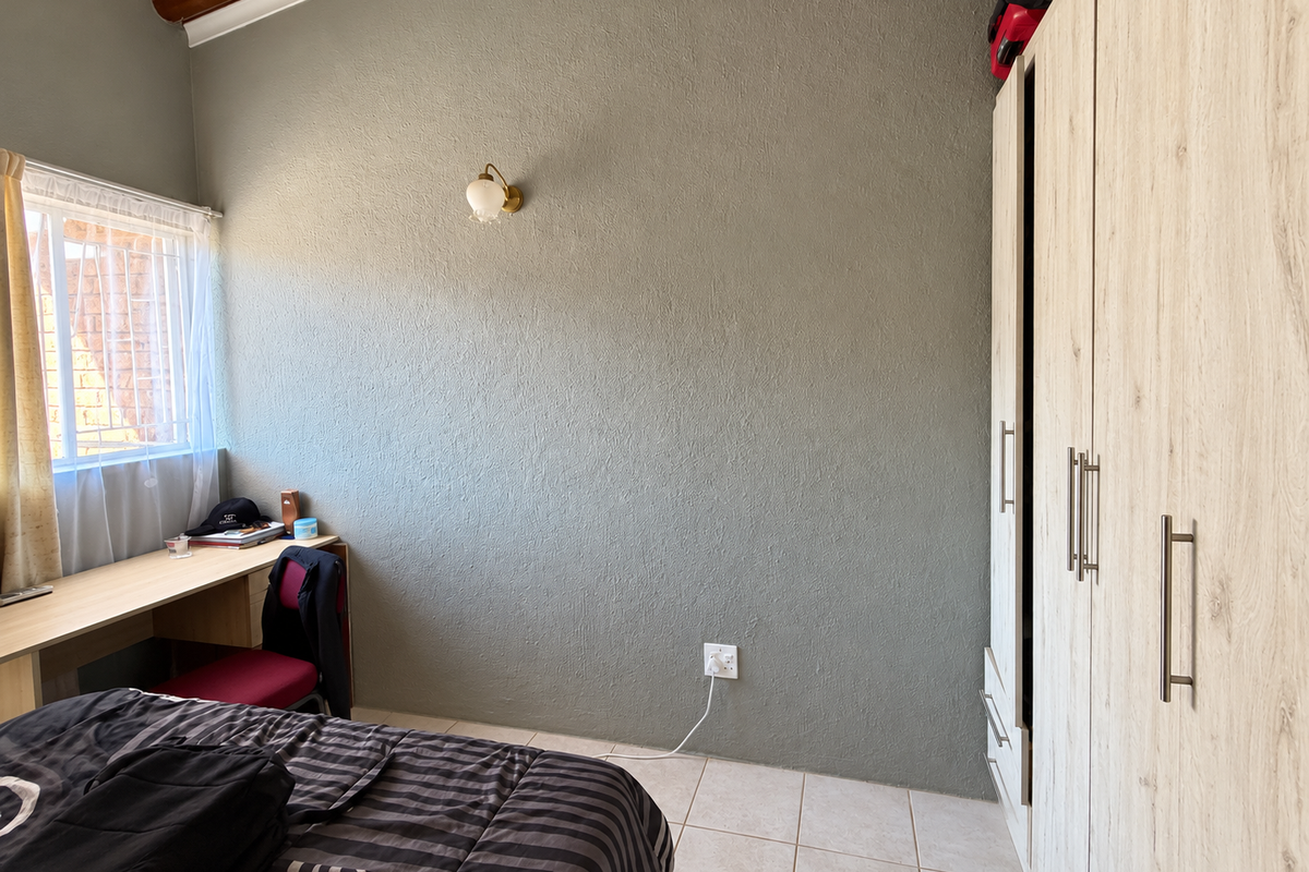 A functional bedroom featuring tiled flooring, a built-in wardrobe, a built-in desk, and a wall-mounted light fixture.