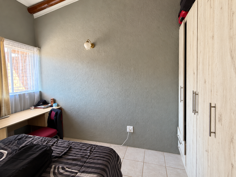 A functional bedroom featuring tiled flooring, a built-in wardrobe, a built-in desk, and a wall-mounted light fixture.