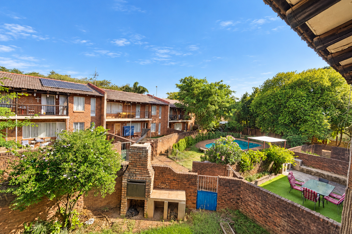 Elevated view of a townhouse complex rear garden featuring a built-in braai, communal swimming pool, and brick boundary walls.