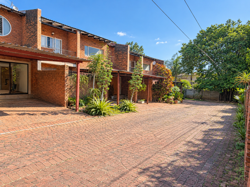 Front exterior view of a townhouse complex featuring a paved driveway, covered carport, and classic red brick facade with established landscaping.