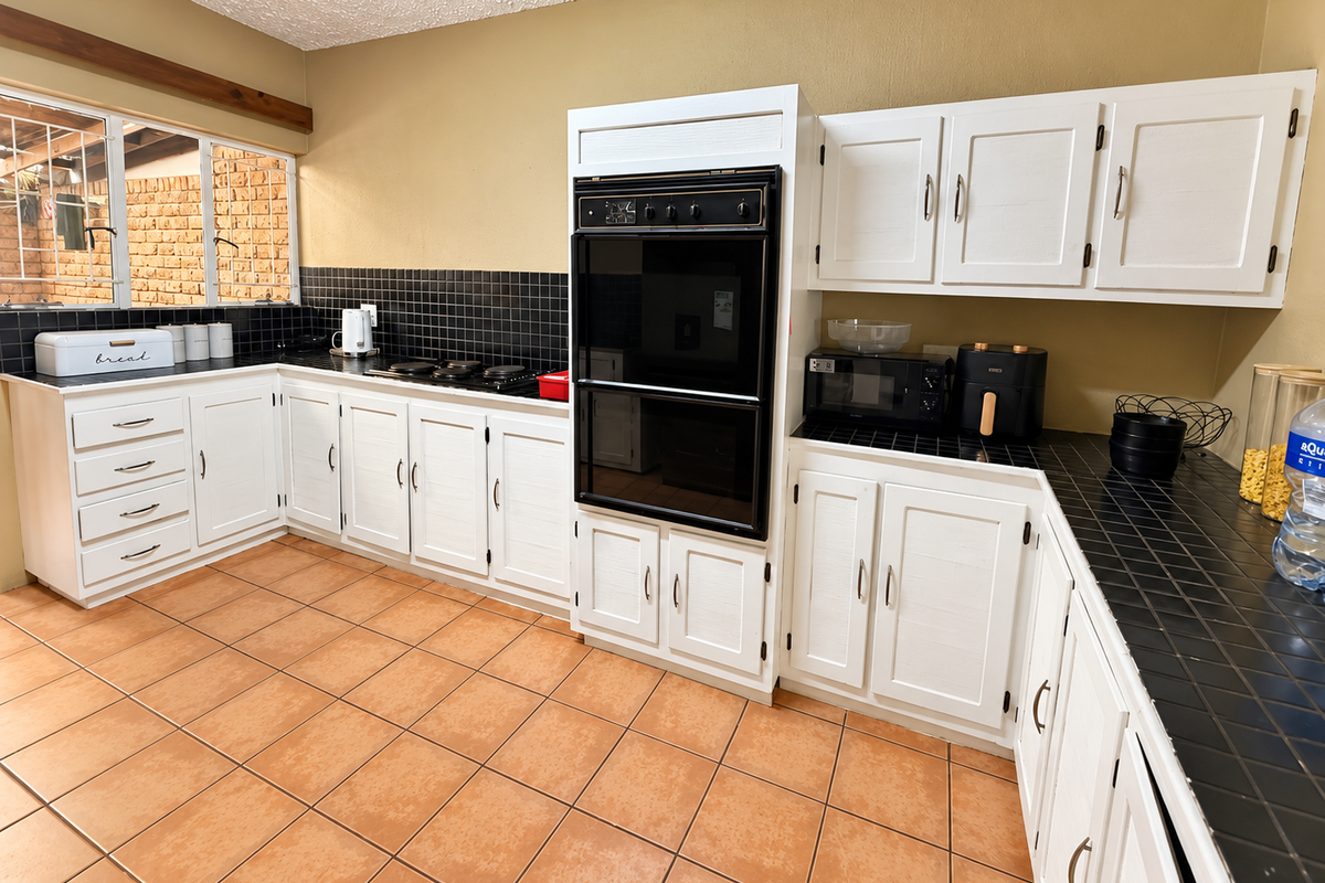 A functional kitchen featuring white cabinetry, black tiled countertops, a built-in oven, and ceramic floor tiles, offering a classic layout with ample storage space.