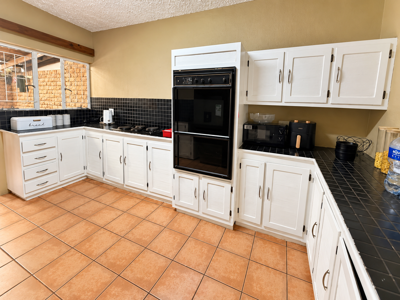 A functional kitchen featuring white cabinetry, black tiled countertops, a built-in oven, and ceramic floor tiles, offering a classic layout with ample storage space.