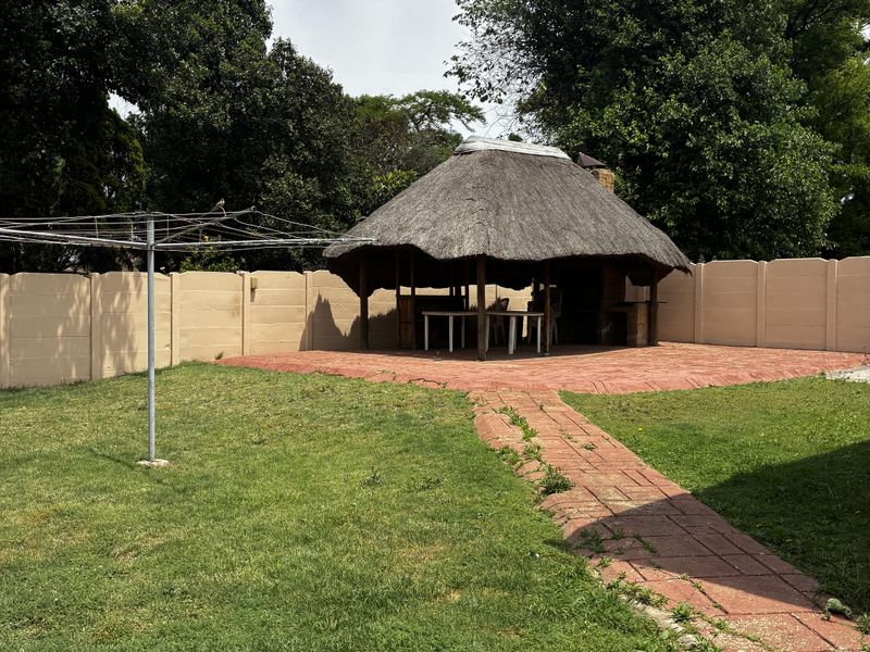 Spacious backyard featuring a traditional thatched lapa, brick paved patio area, and a well-defined pathway, enclosed by a secure precast concrete boundary wall.