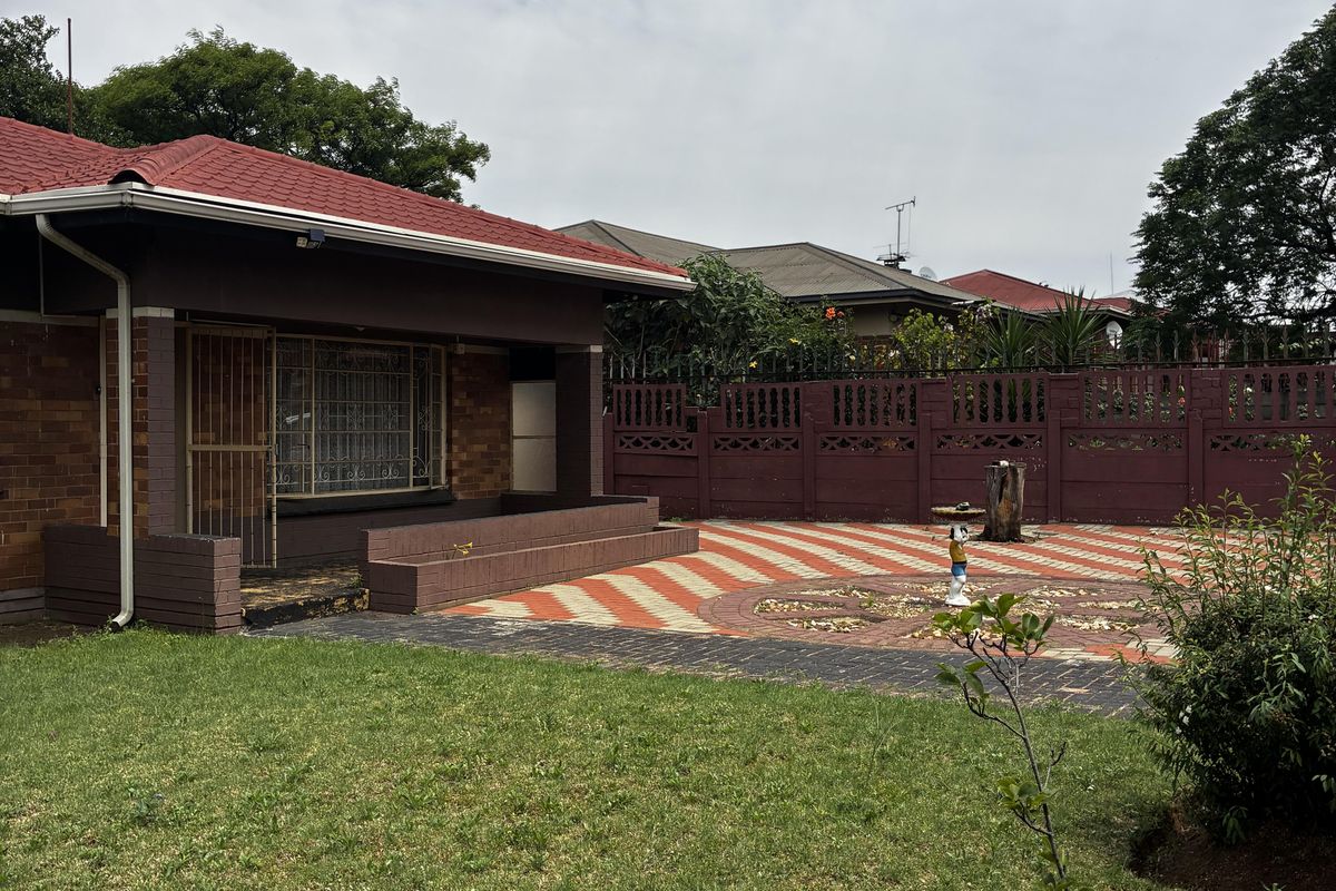 Rear view of the house featuring a paved patio area, brick facade, tiled roof, and a well-maintained garden with boundary walling.